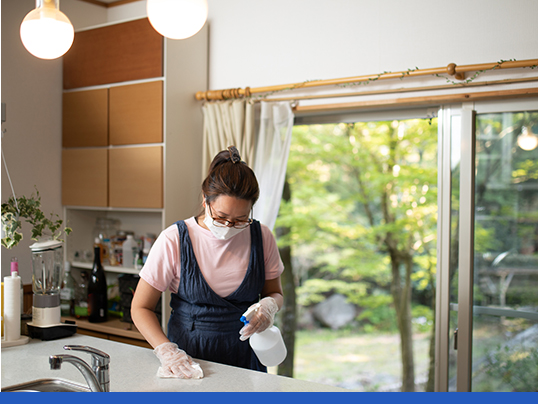 Mulher usando máscara facial e luvas de proteção limpa bancada de cozinha